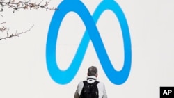 FILE - A person stands in front of a Meta sign outside of the company's headquarters in Menlo Park, Calif., March 7, 2023. 