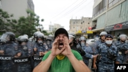 FILE - A protester wearing a scarf of the Shi'ite Hezbollah movement chants slogans while being watched by Lebanese police during an anti-U.S. rally near the United States' embassy building in Awkar, northeast of Lebanon's capital Beirut, July 10, 2020.