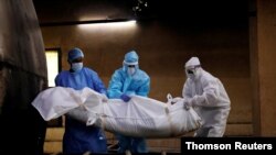 FILE - A health worker and relatives wearing personal protective equipment carry the body of a man who died from COVID-19 for his cremation at a crematorium in New Delhi, India, Aug. 17, 2020.