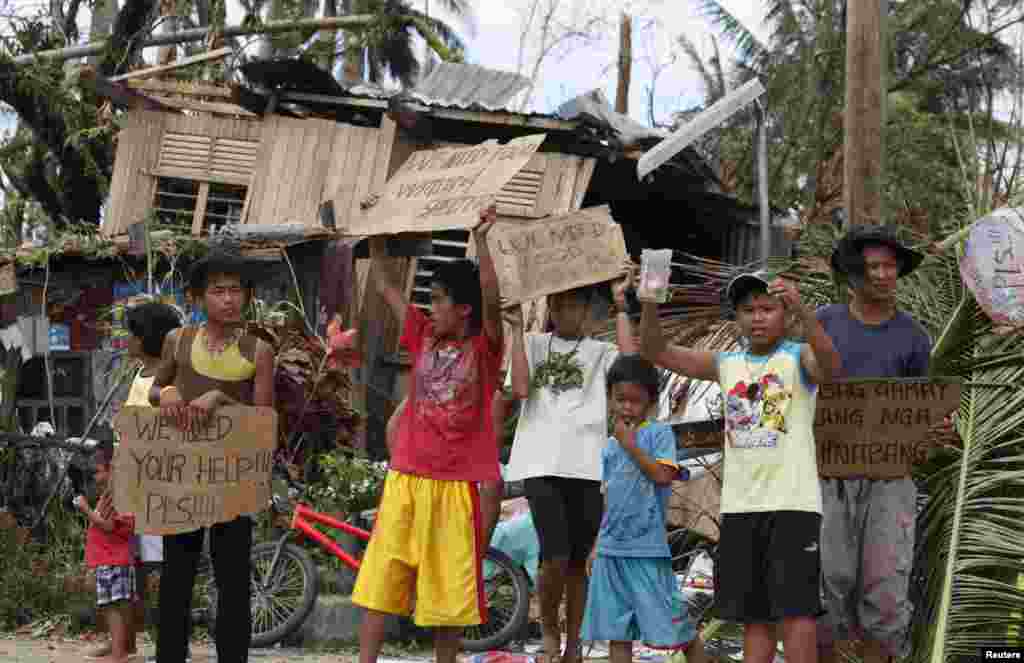 Anak-anak memegang papan bertuliskan permintaan bantuan dan makanan di pinggir jalan kota Tabogon, provinsi Cebu, yang dihantam topan Haiyan (11/11). (Reuters/Charlie Saceda)