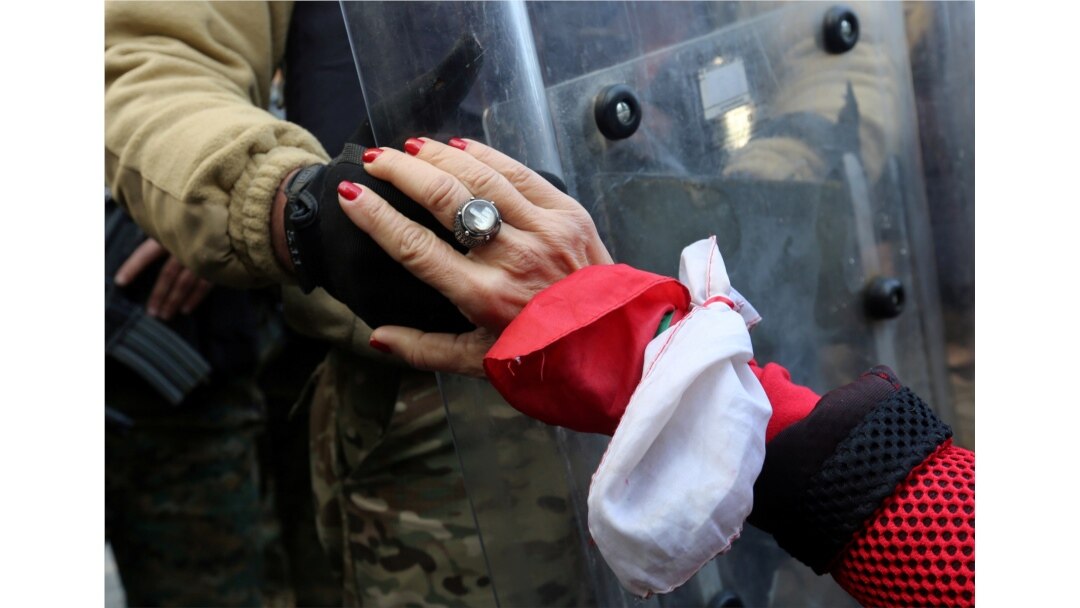 A protester holds the hand of a Lebanese army soldier during a protest against the political elite in Beirut, Jan. 27, 2020.