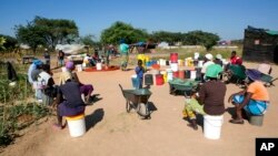 FILE - Women and children wait for their turn to fetch water in a poor suburb of Harare, Zimbabwe, March, 31, 2020.