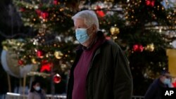 গ্রীসের এথেন্সের সিন্টাগমা স্কোয়ারে ক্রিসমাস ট্রি'র সামনে দিয়ে একজন বয়স্ক মানুষ মাস্ক পরে হেঁটে যাচ্ছেন। ডিসেম্বর ০১, ২০২১। 