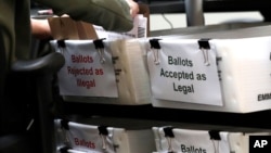 FILE - A Miami-Dade County Elections Department employee places a vote-by-mail ballot for the August 18 primary election into a box for rejected ballots at the Miami-Dade County Elections Department, in Doral, Florida, July 30, 2020.