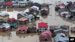 FILE - Flood-affected people row boats past partially submerged buildings in floodwaters in Srinagar, India, Sept. 9, 2014. 