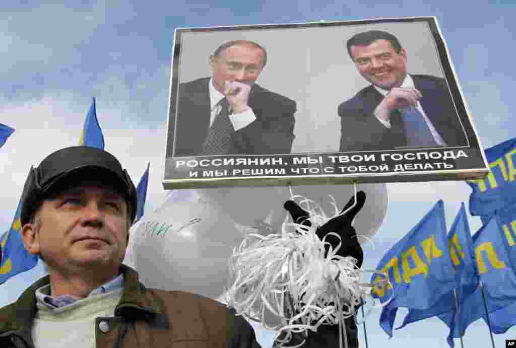 A protester holds a placard with a picture of Russian President Dmitry Medvedev (R) and Prime Minister Vladimir Putin during a demonstration in the southern Russian city of Stavropol, December 24, 2011. The placard reads: "Russians, we are your lords, and