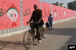 Seorang pengendara sepeda melewati sebuah tembok yang digambari simbol partai Muttahida Qaumi Movement menjejlang pemilihan umum di Karachi, Pakistan. 5 Januari 2024. (Foto: Asif Hassan/AFP)