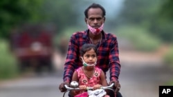 An Indian villager and a child wearing masks on their chin ride on a bicycle on the outskirts of Gauhati, India, June 7, 2021. (