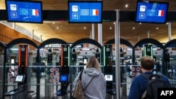 FILE - Police officers help passengers to go through a facial recognition verification system at Roissy-Charles de Gaulle airport, north of Paris, on July 3, 2024.