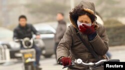 Seorang perempuan mengenderai sepeda sambil mengenakan masker di tengah asap kabut di Beijing, China (foto: dok).