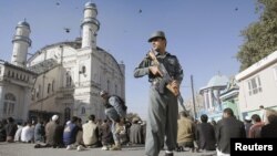 Seorang polisi Afghanistan berjaga saat warga menunaikan ibadah sholat Idul Adha di luar mesjid Shah-e-Dushamshera di Kabul, Afghanistan (26/10).