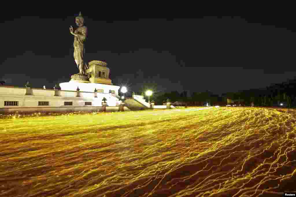 Buddhists holding candles encircle a large Buddha statue during Makha Bucha Day at a temple in Nakhon Pathom province on the outskirts of Bangkok, Thailand.