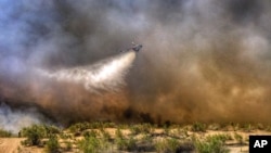 This photo provided by the San Bernardino County Fire Department shows a helicopter making a drop on a wildfire that started in western Arizona and jumped the Colorado River into California, near Needles, Calif., April 6, 2016.