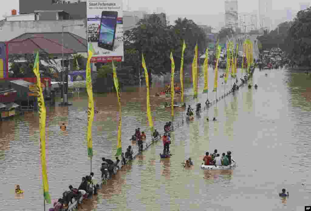 Warga mengarungi jalanan yang banjir di Jakarta, Senin (13/1). (AP/Achmad Ibrahim)