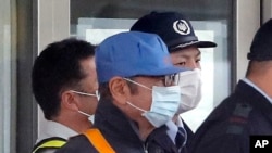 Pria mengenakan masker bertopi biru, diyakini mantan Ketua Nissan Carlos Ghosn, dikawal penjaga keamanan keluar dari Pusat Penahanan Tokyo di Tokyo, Rabu, 6 Maret 2019, setelah membayar uang jaminan sebesar 1 miliar yen ($ 8,9 juta). 