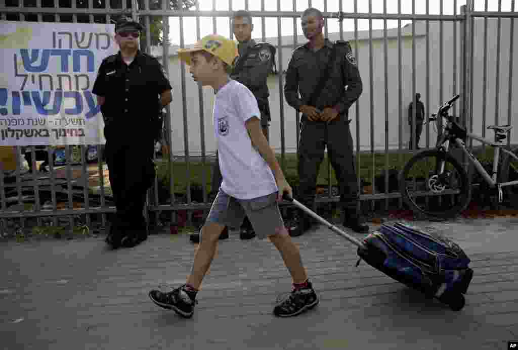 An Israeli student pulls his bag on his way to elementary school as he walks past policemen in the coastal city of Ashkelon, Sep. 1, 2014.