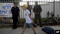 FILE - An Israeli student pulls his bag on his way to elementary school as he walks past policemen in the costal city of Ashkelon, Sep. 1, 2014.