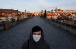A young man wearing a face mask walks across an empty Charles Bridge in Prague, Czech Republic, Monday, March 16, 2020.