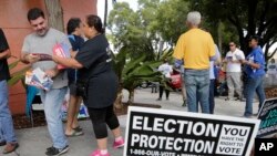 Ingrid Vaca, de Falls Church, en Virginie, bénévole de protection électorale, deuxième à partir de la gauche, remet à un électeur une brochure sur les droits des votants, à l'extérieur d'un bureau de vote à l'auditorium du comté de Miami-Dade, à Miami, 8 