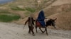 An Afghan man walks with a burqa-clad woman and children riding a donkey along a hillside in the Argo district of Afghanistan's Badakhshan province on October 12, 2026.