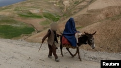 An Afghan man walks with a burqa-clad woman and children riding a donkey along a hillside in the Argo district of Afghanistan's Badakhshan province on October 12, 2026.