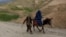 An Afghan man walks with a burqa-clad woman and children riding a donkey along a hillside in the Argo district of Afghanistan's Badakhshan province on October 12, 2026.