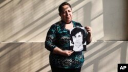 In this Sept. 6, 2018 photo, 54-year-old teacher Vittoria E Natto poses for a portrait inside her high school holding a photo of herself when she was 9 years old, in Santiago, Chile.