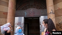 FILE - People wearing face masks stand outside the damaged entrance of the Association of Banks, in Beirut, Lebanon, Aug. 21, 2020.