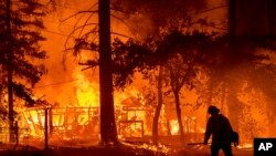 Seorang petugas pemadam kebakaran melewati rumah yang terbakar saat Dixie Fire berkobar di Plumas County, California, 24 Juli 2021. (AP Photo/Noah Berge)