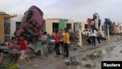 Warga berdiri di luar rumah-rumah mereka yang rusak akibat hantaman mobil yang dibawa tornado di kota Ciudad Acuna, negara bagian Coahuila, Meksiko (25/5). (Reuters/Ramiro Gomez)