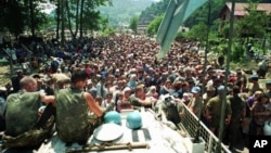 FILE - Dutch U.N. peacekeepers sit on top of an armored personnel carrier as Muslim refugees from Srebrenica, eastern Bosnia, gather in the nearby village of Potocari, July 13, 1995.