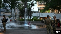 Los soldados hacen guardia mientras un niño juega en una fuente en la plaza Cívica del centro histórico de San Salvador el 1 de octubre de 2024.