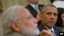 Perezida wa Amerika, Barack Obama, i buryo, ariko yumviriza umuhsikiranganaji wa mbere w'Ubuhindi, Narendra Modi ariko yishura ibibazo vy'abamenyeshamakuru mu gihe c'inama hagati y'abo bategetsi babiri mu ngoro kwa perezida, Maison Blanche i Washington, kw'italiki indwi, ukwezi kwa gatandatu, umwaka w'i 2016.