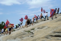 FILE - In this Aug. 1, 2015, photo, Confederate flag supporters climb Stone Mountain to protest what they believe is an attack on their Southern heritage, during a rally at Stone Mountain Park in Stone Mountain, Ga.