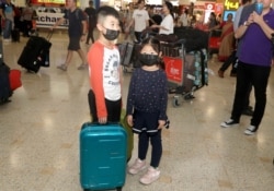 Children, wearing face masks, wait for their mother after arriving in Sydney, Jan. 23, 2020, from a flight from Wuhan, China.