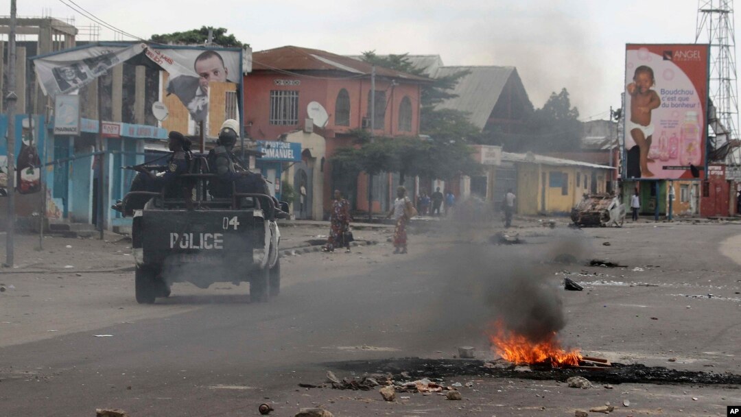 Kendaraan polisi melewati sampah yang dibakar dalam protes-protes di Kinshasa, Republik Demokratik Kongo (20/12). (AP/John Bompengo)