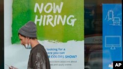 FILE - A man walks past a "Now Hiring" sign on a window at a Sherwin Williams store, in Woodmere Village, Ohio, Feb. 26, 2021.