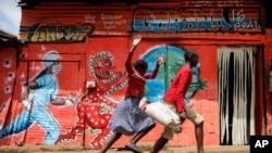 Children run down a street past an informational mural warning people about the dangers of the COVID-19 coronavirus, in the Kibera slum of Nairobi, Kenya on Wednesday, June 3, 2020. (AP Photo/Brian Inganga)