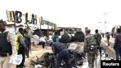 Somali security officers assess the wreckage of a car destroyed at the scene of an explosion in Mogadishu, Somalia, July 13, 2020. 