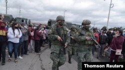 에콰도르 고토팍시주 교도소에 폭동이 일어난 뒤 수감자 가족들이 지난 22일 가족 소식을 기다리고 있는 교도소 앞에 무장 경찰이 지나가고 있다. 