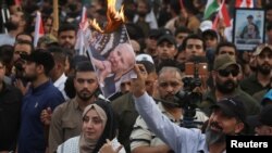 A demonstrator burns a printout of U.S. President Joe Biden, as supporters of Iraqi Shiite armed groups gather to protest against the U.S. for supporting Israel, Oct. 20, 2023. 