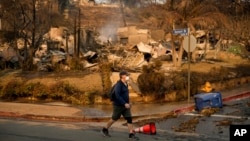 Čovek prolazi pored uništene kuće u naselju Pacifik Palisejds, 10. januar 2025. (AP Photo/John Locher)
