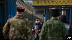 A woman walks with a baby as members of the Crimean self defense forces stand on the platform at the main railway station in Simferopol, Ukraine, March 14, 2014. 