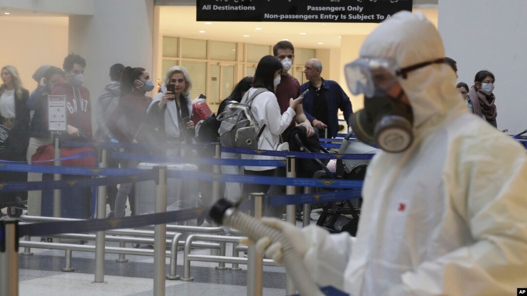ILUSTRACIJA - Putnici na aerodromu dok osoblje vrši dezinfekciju od virusa (Foto: AP/Hassan Ammar)
