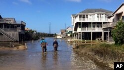 A couple walk along a road flooded with sea water brought by Hurricane Maria in Buxton, N. C., Sept. 27, 2017. Maria has weakened to a tropical storm and is headed east, northeast away from North Carolina.