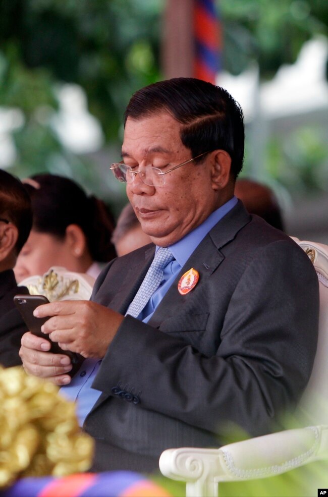 FILE - Cambodia's Prime Minister Hun Sen holds a mobile device during the celebrations of the 65th anniversary of the ruling Cambodian People 's Party in Phnom Penh, Cambodia, Tuesday, June 28, 2016.