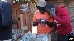 FILE: In this photo taken Thursday, Aug. 8, 2019, vendors are seen on their mobile phones while selling cash in Harare, Zimbabwe. With inflation soaring and cash in short supply, many Zimbabweans transfer funds using their mobile phones and pay a premium to get currency.(AP Photo