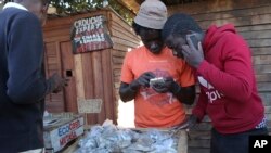 In this photo taken Thursday, Aug. 8, 2019, vendors are seen on their mobile phones while selling cash in Harare, Zimbabwe. (AP Photo/Tsvangirayi Mukwazhi)