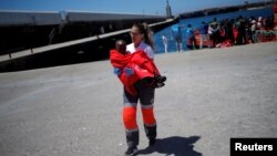 Seorang anak migran dari kapal yang dicegat di lepas pantai Selat Gibraltar, dibopong oleh seorang anggota Palang Merah Spanyol, setibanya di pelabuhan Tarifa, Spanyol selatan, dengan kapal penyelamat, 4 Juli 2018. (Foto: dok).