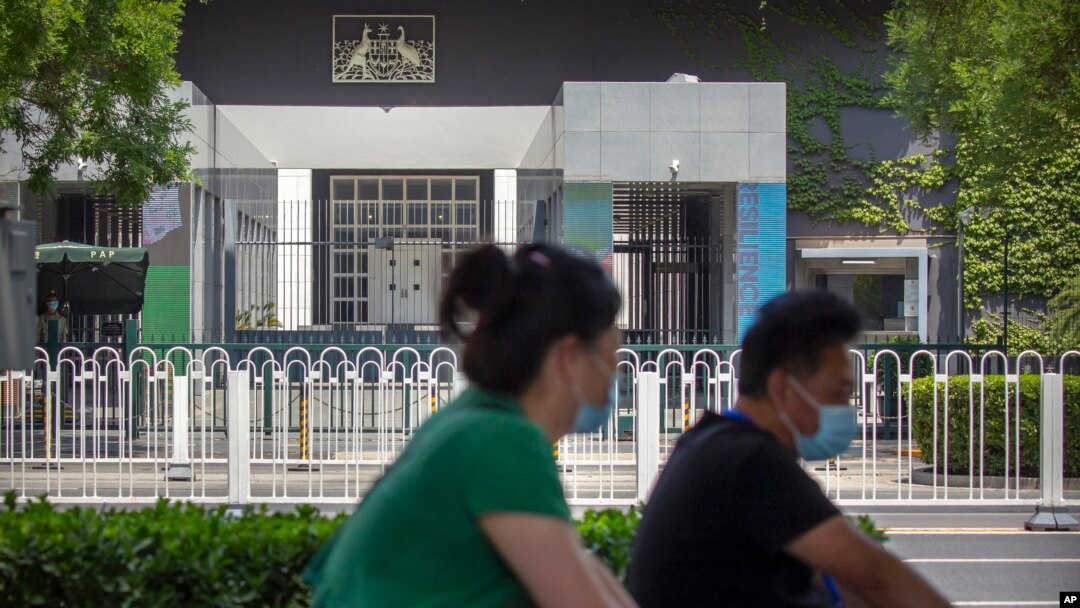 People wearing face masks to protect against the new coronavirus ride past the Australian Embassy in Beijing, June 6, 2020. 